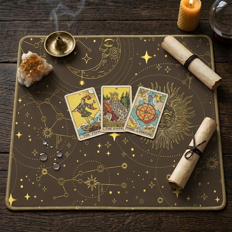 Peut inclure: Un tapis de tarot marron avec des motifs c&eacute;lestes dor&eacute;s, dont des &eacute;toiles, des lunes et des soleils. Trois cartes de tarot sont affich&eacute;es, ainsi que des parchemins roul&eacute;s, une bougie et un cristal. Le tapis est rectangulaire avec une bordure dor&eacute;e.