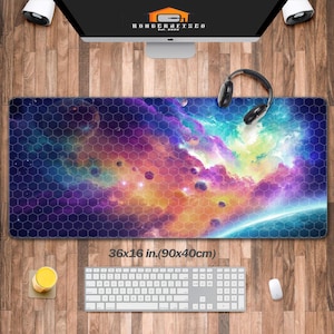 May include: A rectangular desk mat featuring a vibrant space nebula design with purple, blue, and yellow hues overlaid by a dark hexagonal grid pattern. The mat includes printed text stating 36x16 in. (90x40cm) and a pair of black headphones.