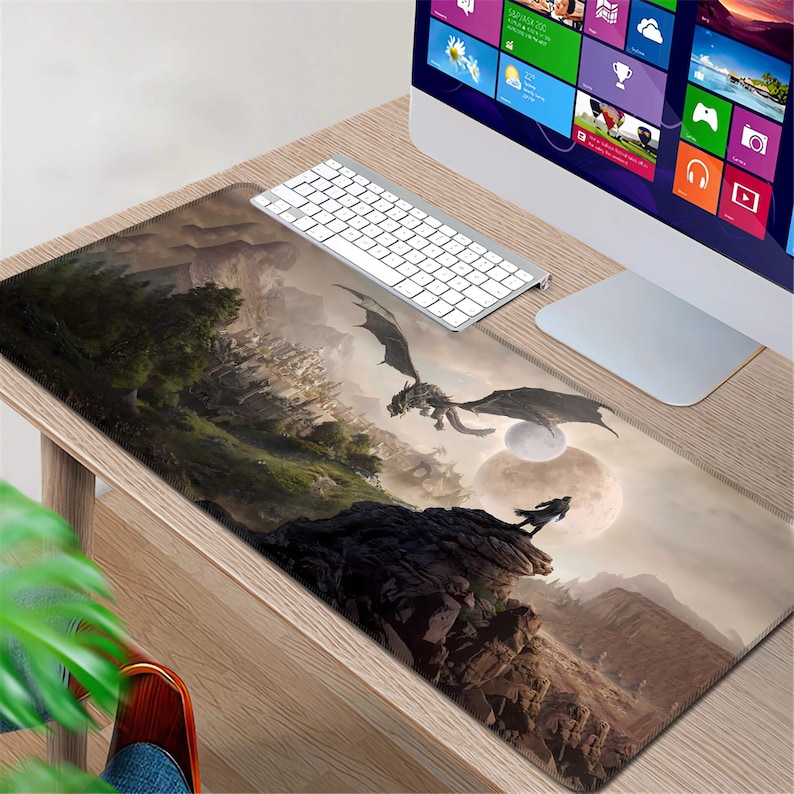 K&ouml;nnte beinhalten: Eine Fantasy-Mausmatte mit einem dunkelgrauen Drachen, der &uuml;ber eine felsige Landschaft mit einem Mond im Hintergrund fliegt. Die Mausmatte liegt auf einem Holztisch mit einer Tastatur und einem Computermonitor.