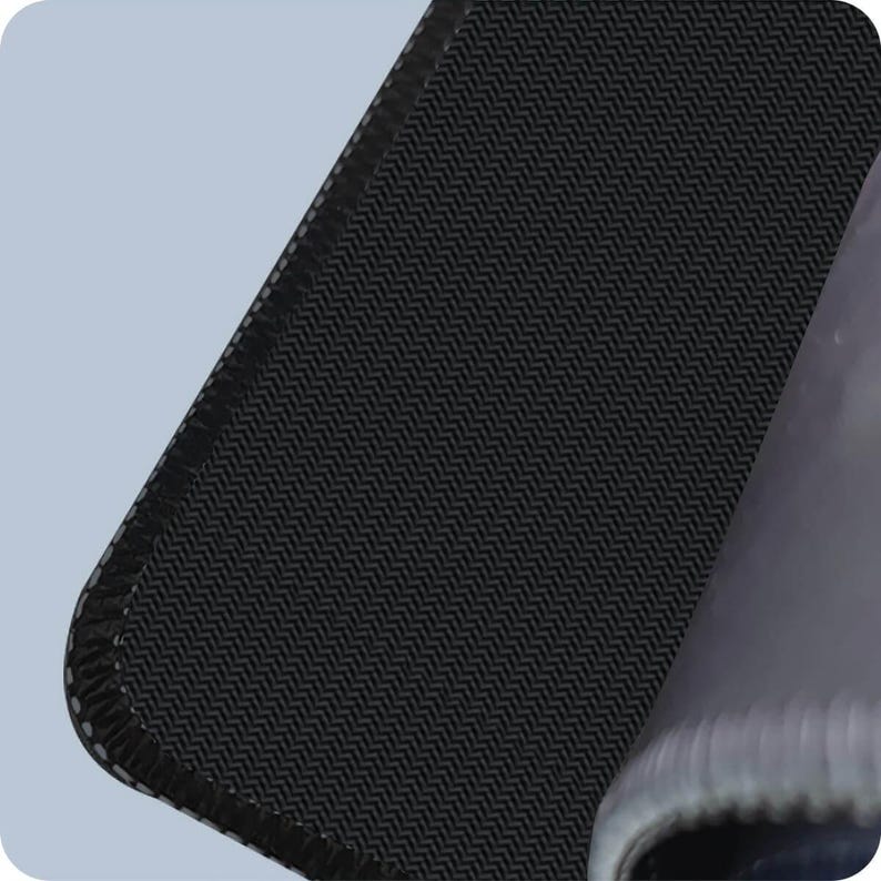Peut inclure: Gros plan sur un tapis de souris noir avec une surface textur&eacute;e. Le tapis a une bordure cousue et un dessous antid&eacute;rapant. Le coin du tapis est l&eacute;g&egrave;rement pli&eacute;, r&eacute;v&eacute;lant le dessous.