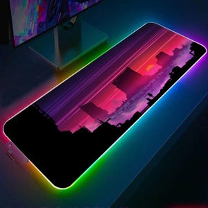 May include: A rectangular gaming mouse mat featuring a sunset scene in pinks, purples, and oranges. The mat has a black cityscape silhouette and a colourful LED edge with a rainbow gradient.