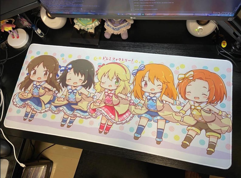 May include: A rectangular mousepad featuring five anime-style characters in colorful outfits. The characters are holding hands and smiling, set against a pastel background with the text "ドレミファクトリー!".
