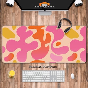 Könnte beinhalten: Eine Schreibtischmatte mit abstraktem Design in Rosa, Orange und Gelb auf beigefarbenem Hintergrund. Die Matte misst 36x16 Zoll (90x40 cm).
