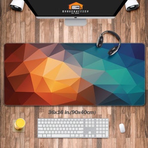 May include: A large rectangular mouse mat with a geometric design in shades of orange, yellow, blue, and green. The mat measures 90 x 40 cm. A keyboard, mouse, and headphones are on the wooden surface.