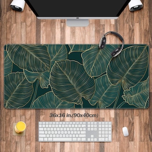 Puede incluir: Un alfombrilla de ratón con estampado de hojas verdes y doradas con borde cosido. La alfombrilla de ratón mide 36x16 pulgadas (90x40 cm).