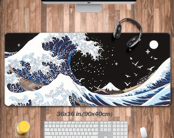 May include: A large rectangular desk mat featuring a Japanese wave design in shades of blue and white against a black background. The mat measures 36 x 16 inches. A keyboard, mouse, and headphones are also visible.