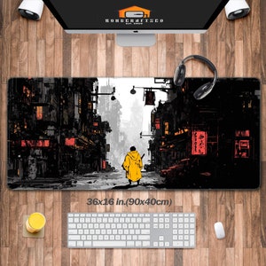 Puede incluir: Alfombrilla de escritorio rectangular con una ilustración de paisaje urbano en tonos negro, blanco y naranja. El diseño muestra a una persona con un abrigo amarillo caminando por una calle. La alfombrilla mide 90 x 40 cm.