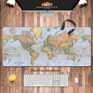 May include: A large desk mat featuring a vintage world map design. The mat is rectangular, measuring 36 x 16 inches, and includes the text "STANDARD'S LIBRARY MAP OF THE WORLD". The mat is surrounded by a computer, headphones, keyboard, mouse, and a drink.