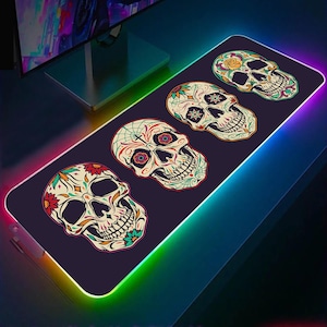 May include: A black gaming mouse pad with a colorful rainbow border. The mouse pad features four sugar skull designs with intricate floral patterns and bright colors.