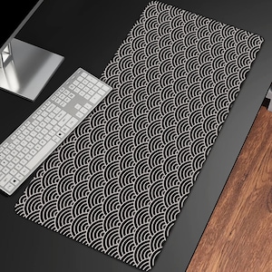 Puede incluir: Una alfombrilla de escritorio en blanco y negro con un patrón de olas repetidas. Un teclado blanco y un monitor de ordenador son visibles en el escritorio. La alfombrilla es rectangular y cubre una gran parte de la superficie del escritorio.