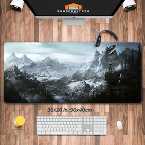 May include: A large, black and white gaming mouse mat featuring a snowy mountain landscape with a lone figure standing on a cliff. The mouse mat measures 36x16 inches (90x40cm).