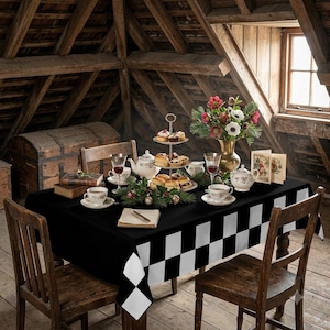Könnte beinhalten: Ein Esstisch mit einer schwarz-weiß karierten Tischdecke, gedeckt mit einer Etagere für Gebäck, einer Teekanne, Teetassen, einer Blumenvase und Büchern, umgeben von Holzstühlen in einem rustikalen Dachbodenambiente.
