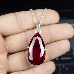 Pode incluir: Um colar de corrente de prata com um grande pingente de pedra vermelha em forma de pêra.