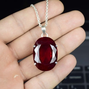 Può includere: Una collana con catena d'argento con un ciondolo di pietra preziosa rossa di forma ovale.