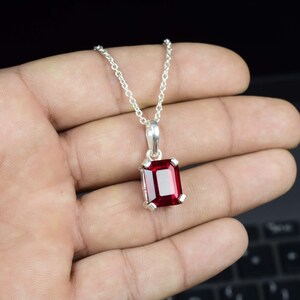 Peut inclure: Un collier en argent avec un pendentif en pierre rouge. Le pendentif est une pierre taillée en émeraude sertie dans une bélière en argent.