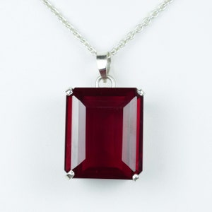 May include: A silver necklace featuring a large, rectangular, deep red gemstone pendant. The pendant is set with four small silver prongs at each corner and hangs from a delicate silver chain. The gemstone has a faceted cut.