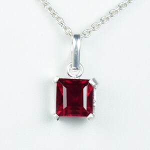 May include: A silver pendant necklace featuring a square, deep red gemstone. The gemstone is set in a silver frame with four prongs. The chain is a delicate silver link chain, and the background is white.
