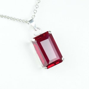 May include: A silver pendant necklace with a large, rectangular, deep red gemstone. The gemstone is set in a silver bezel and hangs from a delicate silver chain. The pendant has a polished, reflective surface, and the chain is a classic link style.