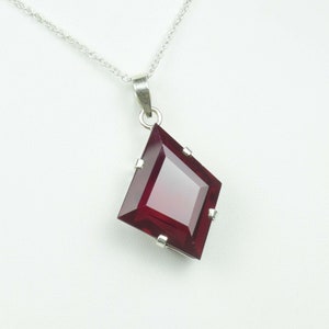 Op de afbeelding: Een zilveren ketting met een hanger met een grote, gefacetteerde, donkerrode edelsteen in een vierkante vorm.