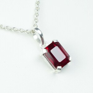 May include: A silver necklace featuring a rectangular, deep red gemstone pendant. The pendant is set in a silver bezel and hangs from a delicate silver chain. The gemstone has a polished, reflective surface.