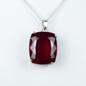 May include: A silver chain necklace with a large, red, faceted gemstone pendant.