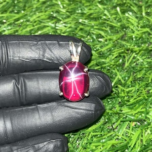 Puede incluir: Un colgante de plata con una piedra preciosa de rubí estrella roja con un patrón de estrella.