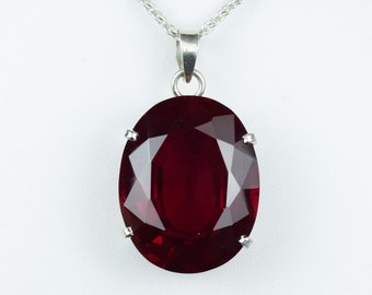 Op de afbeelding: Een zilveren ketting met een grote, ovale, rode edelsteen hanger.