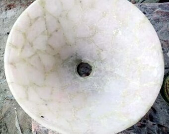 Puede incluir: Un lavabo redondo de piedra blanquecina con un orificio de desagüe central. El lavabo tiene un aspecto veteado con sutiles vetas verdes en toda la superficie. La forma general es circular, adecuado para un baño.