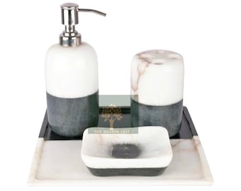 May include: A marble bathroom set with a soap dispenser, toothbrush holder, and soap dish. The set is on a marble tray with a black border. The soap dispenser has a silver pump. The toothbrush holder has three holes for toothbrushes. The soap dish is rectangular. The set is white and gray.