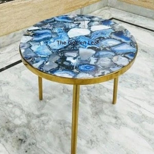 May include: A round side table with a blue agate top and gold metal legs. The table top has a unique pattern of blue and grey agate.