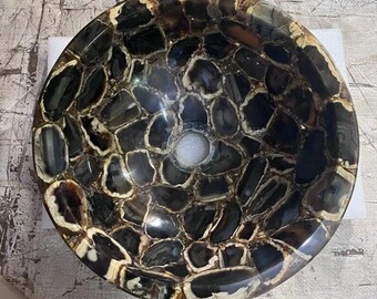 May include: A round, black and white agate stone sink with a drain hole in the center. The sink is made of natural stone and has a unique, organic pattern.