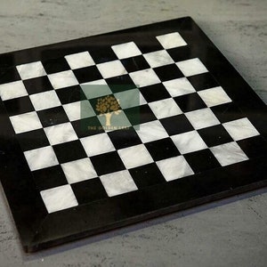 May include: Square black and white marble chessboard. The board features a classic checkerboard pattern with alternating black and white squares. The board is made of marble and has a black border. A classic game board for chess or checkers.