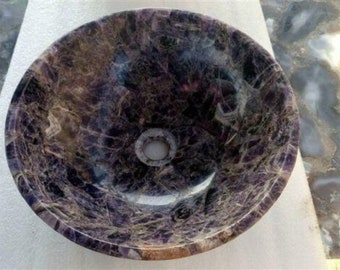 Puede incluir: Un lavabo de piedra de color morado y gris de forma circular con un agujero de drenaje en el centro.