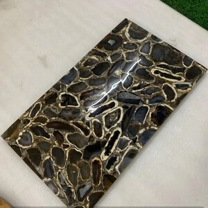 May include: A rectangular tile made of agate, featuring a pattern of brown, black, and white agate slices. The tile has a polished, glossy finish.