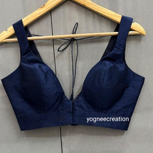 May include: A navy blue sleeveless blouse with a deep V-neckline and a tie closure at the back. The blouse has a fitted bodice and a straight hemline. The text "yogneecreation" is visible on the bottom right corner of the blouse.