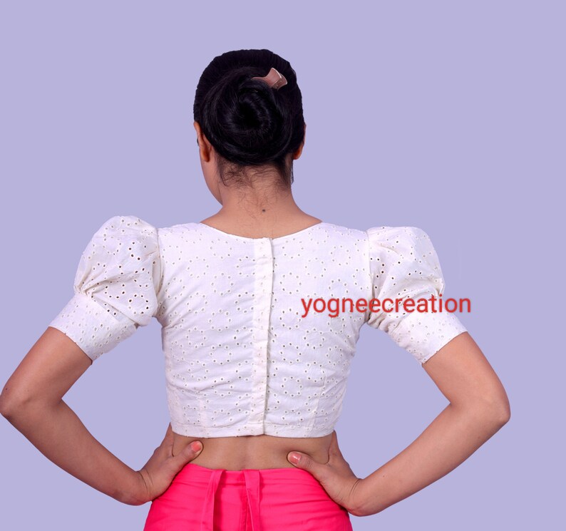 Puede incluir: Blusa blanca de ojal con mangas cortas abullonadas y espalda abotonada. La blusa tiene un dise&ntilde;o perforado delicado y se usa con una prenda rosa. El texto "yogneecreation" es visible.