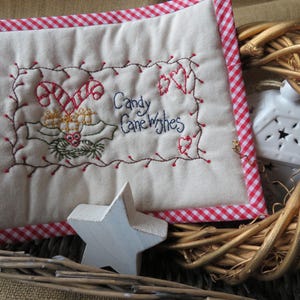May include: A white quilted pillow with a red and white gingham border. The pillow is embroidered with a candy cane, holly, and the text "Candy Cane Wishes".