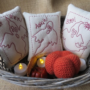 May include: Three white pillow covers with red embroidered ghost designs and the words "EEK!" "AARGH!" and "BOO!"  The pillows are in a wicker basket with orange crocheted pumpkins and white tea lights.