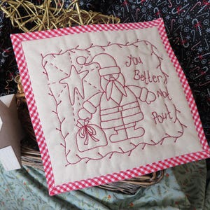 May include: A white fabric square with red gingham trim features an embroidered image of Santa Claus with a bag of gifts and a star. The text "You Better Not Pout" is embroidered in red thread.