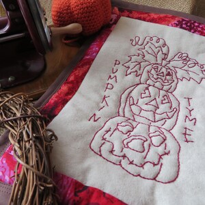 May include: A white fabric panel with red embroidered pumpkins and the words "Pumpkin Thyme" in a stylised font.