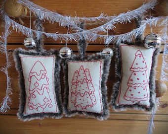 May include: Three handmade Christmas tree ornaments with a white background and red embroidery. Each ornament is trimmed with brown faux fur.