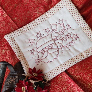 Op de afbeelding: Een wit gestikt kussen met rode stippen en een rode rand. Het kussen heeft een geborduurd ontwerp van Sinterklaas met de tekst "Santa Stop Here".