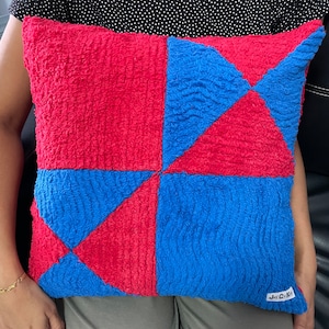 May include: A red and blue square patterned throw pillow with a white tag that says "Joy & Co."