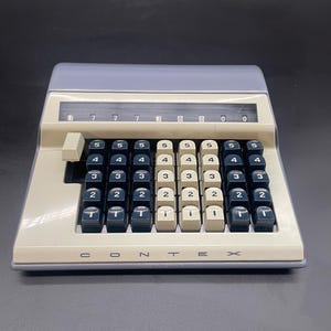 Op de afbeelding: Vintage Contex-rekenmachine met een lichtblauw bovenstuk en een crèmekleurige basis. De rekenmachine heeft zwart-witte toetsen met cijfers en de merknaam "Contex" op de voorkant.