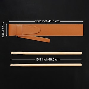 May include: A brown leather drumstick case, 16.3 inches (41.5 cm) long, with a flap closure and a carrying strap. Two wooden drumsticks, each 15.9 inches (40.5 cm) long, are positioned below the case against a black background.
