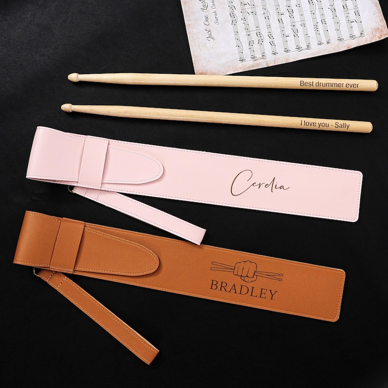 May include: Two pairs of wooden drumsticks with text, "Best drummer ever" and "I love you - Sally". Two personalized drumstick cases, one pink with "Cerelia" and one brown with "BRADLEY" and a drumstick graphic.