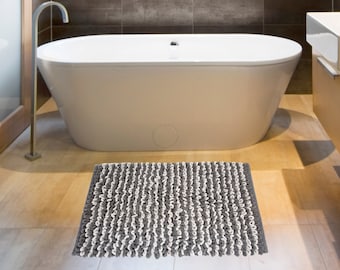 May include: A gray and white bath mat with a textured, looped design. The mat is placed in front of a white bathtub in a modern bathroom.