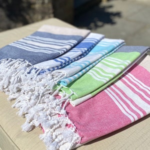 May include: A stack of four striped towels with white fringe. The towels are in shades of blue, green, and pink.