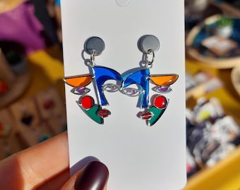 May include: A pair of silver earrings with a blue, green, red, and orange abstract face design.