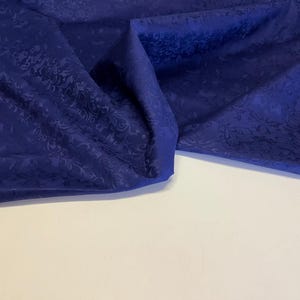 以下が含まれることがあります： 微妙なエンボス加工が施された青い布のクローズアップ。布は折り畳まれ、ドレープされ、その質感と色が際立っています。